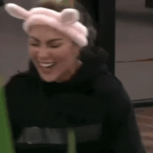a woman wearing a pink headband with bunny ears is smiling and laughing .