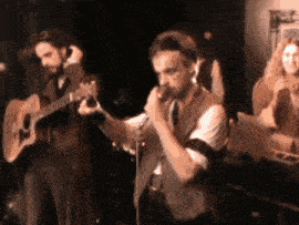 a man singing into a microphone while another man plays guitar
