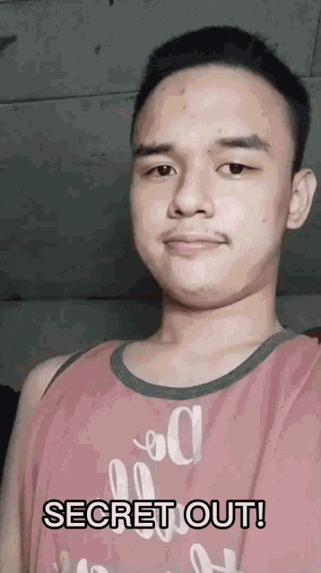 a young man wearing a pink tank top with the words secret out written on it
