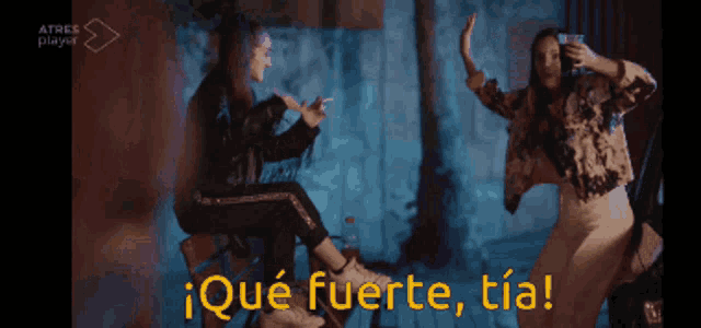 two women are dancing in front of a sign that says ' ique fuerte tia '