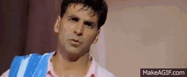 a man wearing a pink shirt and a blue and white towel around his neck is making a funny face .