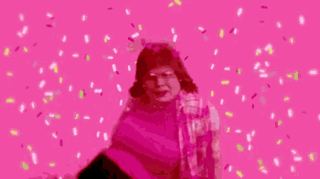 a woman is standing in front of a pink background with sprinkles falling around her .