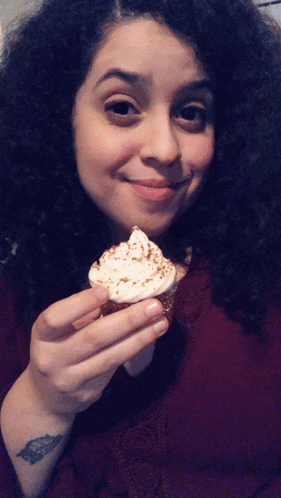 a woman with curly hair holds a cupcake in her hand