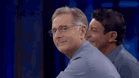 a man wearing glasses is sitting next to another man in a blue shirt .