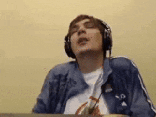 a man wearing headphones and a blue jacket is singing into a microphone .
