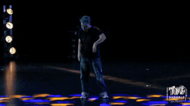 a man in a black shirt is dancing on a stage in front of a sign that says tbc