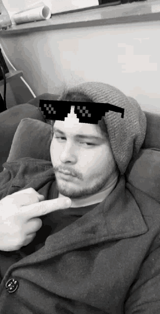 a man wearing a beanie and sunglasses is pointing his finger