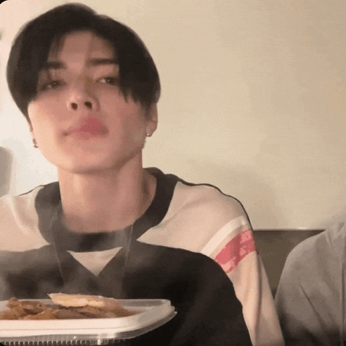 a young man is holding a tray of food and looking at the camera