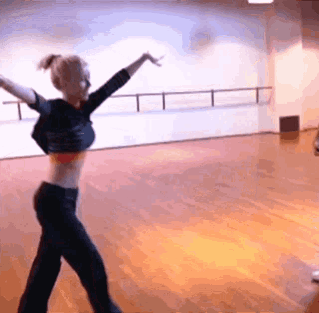 a woman in a crop top and black pants is dancing on a wooden floor