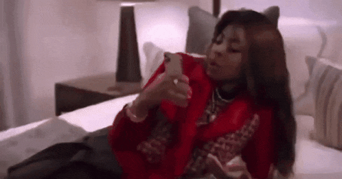 a woman is laying on a bed using a cell phone .