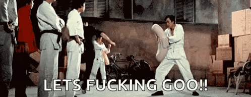 a group of people are standing around a man in a karate uniform holding a pillow .