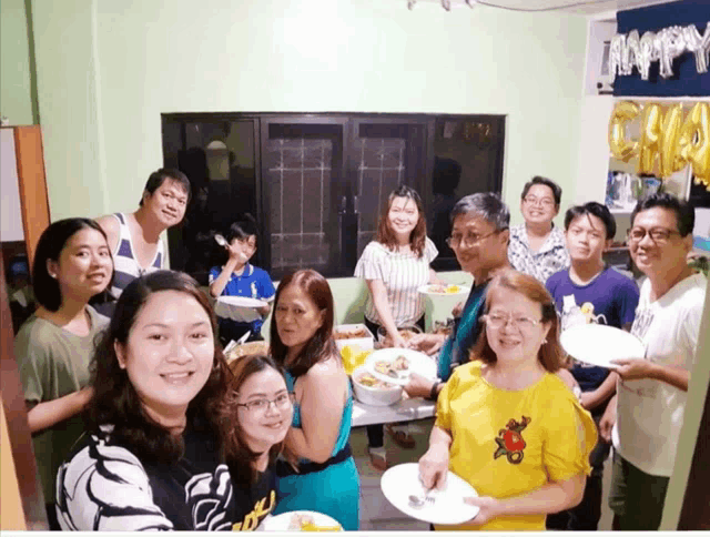 a group of people gathered around a table with plates of food and balloons that say happy birthday