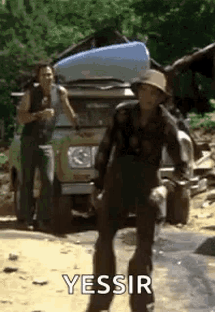 a man in a hat is standing in front of a car with a canoe on top of it .