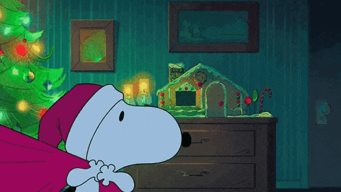 snoopy is wearing a santa hat in front of a gingerbread house and a christmas tree .