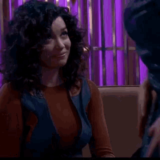 a woman with curly hair is sitting in a chair in front of a purple wall .
