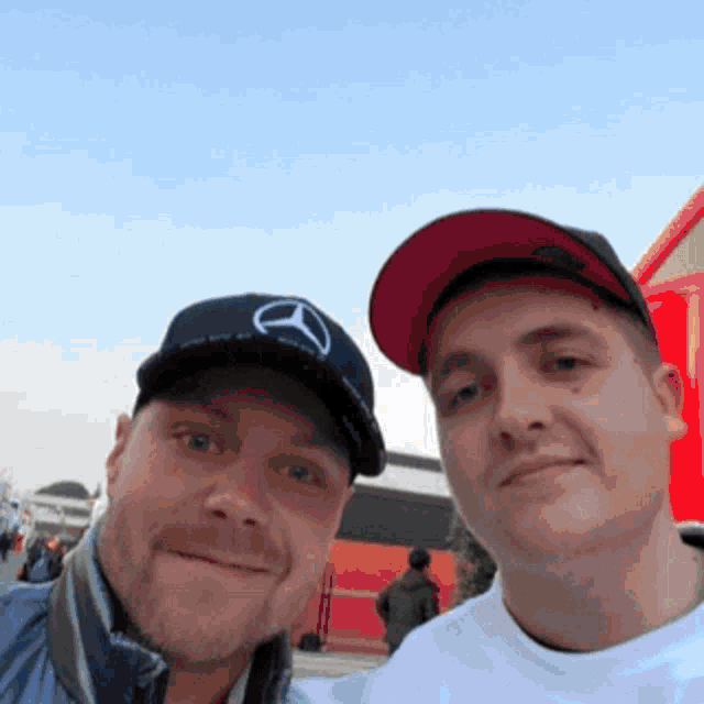 two men are posing for a picture and one has a mercedes logo on his hat