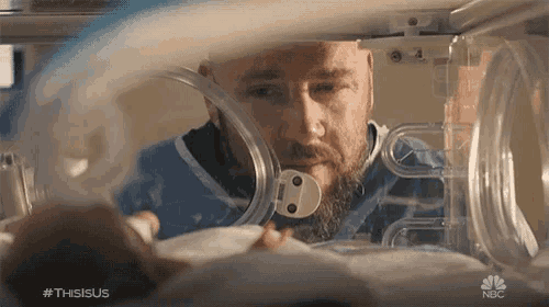 a man with a beard is looking at a baby in an incubator with the hashtag thisisus