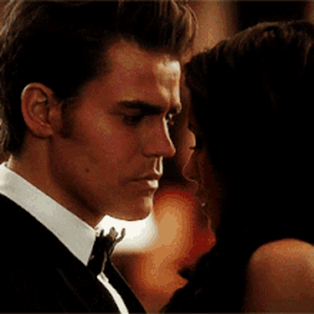 a man in a tuxedo and a woman in a black dress are looking into each other 's eyes