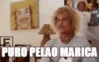 a man with curly hair is sitting in front of a painting of a man and the words puro pelao marica .