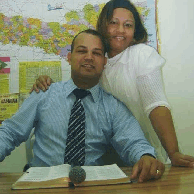 a man and woman are posing for a picture while sitting at a table with a bible and a microphone .