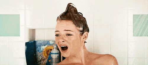 a woman is taking a shower with her hair in a bun and her mouth open .
