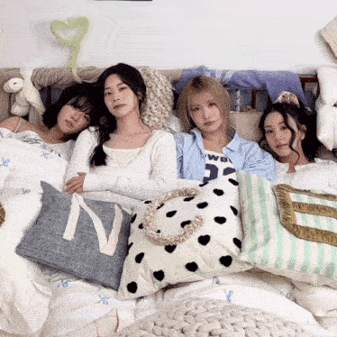 four women are laying on a bed with pillows and one has the letter n on it