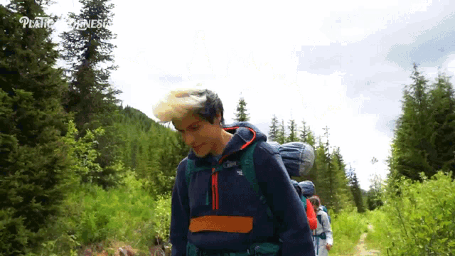 a man wearing a north face jacket walks through a lush green forest