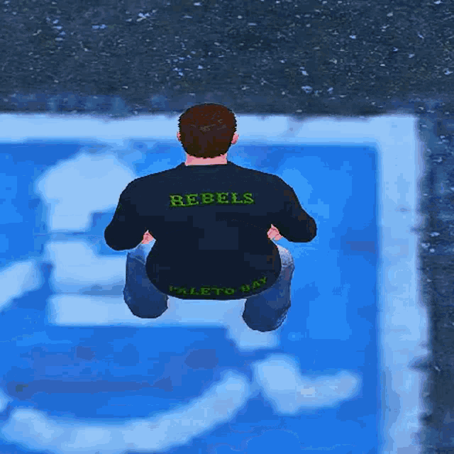 a man wearing a rebels shirt is squatting down in front of a handicapped sign