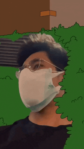a man wearing a face mask and glasses is behind a green bush