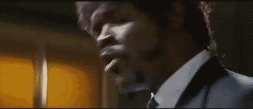 a man in a suit and tie is smoking a cigarette in a dark room .