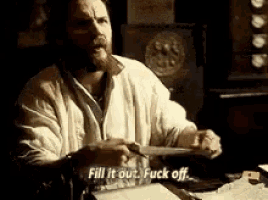 a man with a beard is sitting at a desk holding a knife and saying fill it out fuck off .