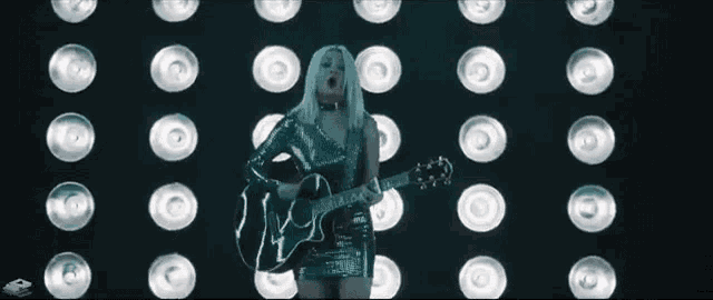 a woman is holding a guitar in front of a wall of lights .