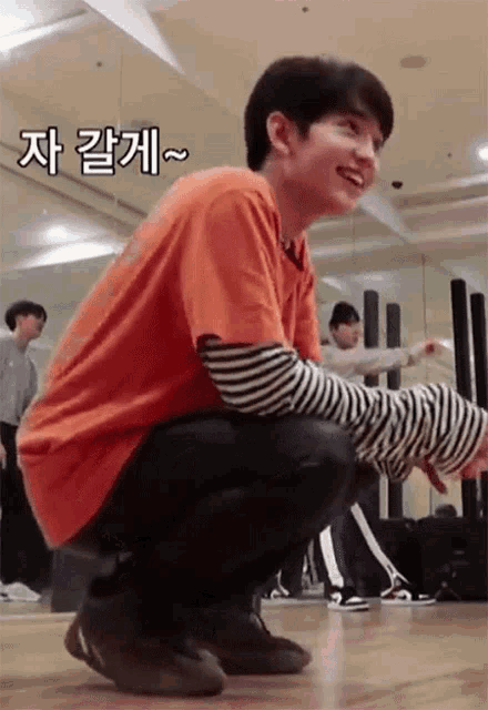 a young man is squatting on the floor in a gym .