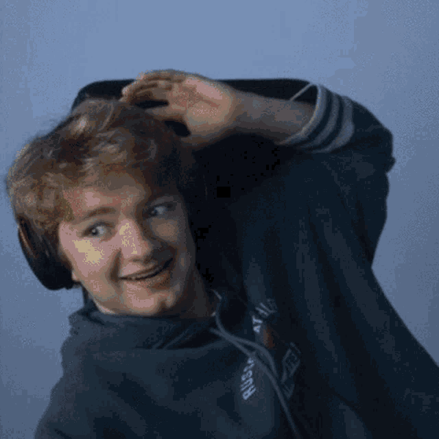a young man wearing headphones and a blue hoodie is smiling while sitting in a chair .