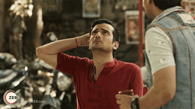 a man in a red shirt stands next to a man in a denim vest with the website www.zees.com visible