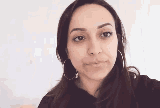 a woman wearing hoop earrings is making a funny face and looking at the camera .