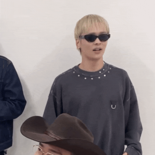 a man wearing sunglasses and a cowboy hat stands next to another man wearing glasses