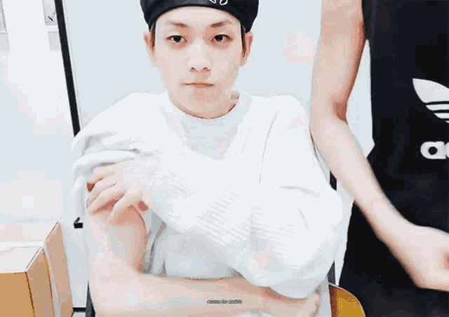 a man wearing a white sweater and a black hat shows off his arm