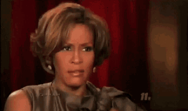 oprah winfrey is sitting in front of a red curtain and wearing a white jacket