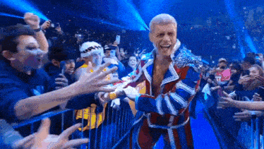 a wrestler in a red , white and blue robe is standing in front of a crowd of people .