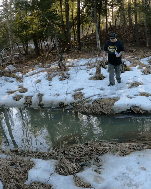 a man wearing a black batman t-shirt is walking through the snow
