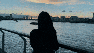 a woman looking out over a body of water with a city in the background