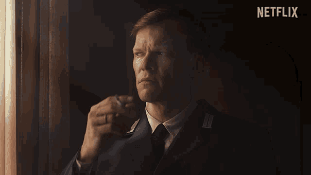 a man in a suit smoking a cigarette with a netflix logo in the background
