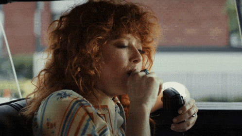 a woman with red curly hair is smoking a cigarette