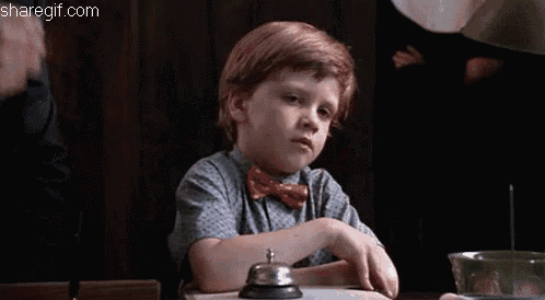 a young boy with red hair is sitting at a table with a bell .