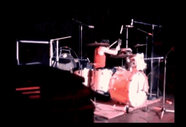 a man in a red shirt is playing drums on a stage in a dark room .