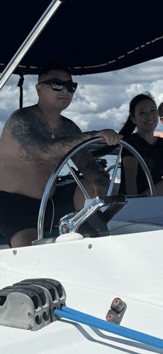 a man without a shirt is driving a boat with a woman behind him