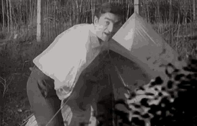 a man is kneeling down in front of a tent in a field .