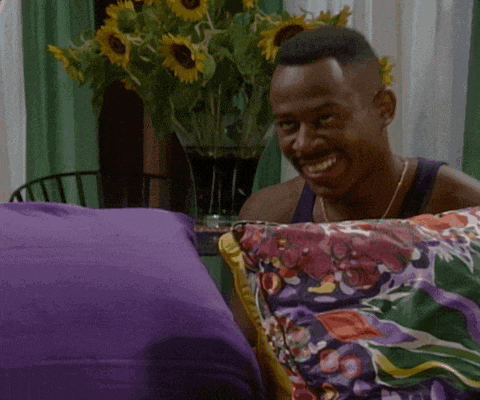 a man is smiling while sitting on a couch with a purple blanket