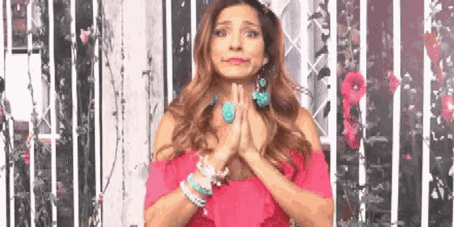 a woman in a pink dress is praying with her hands folded in front of a floral background .